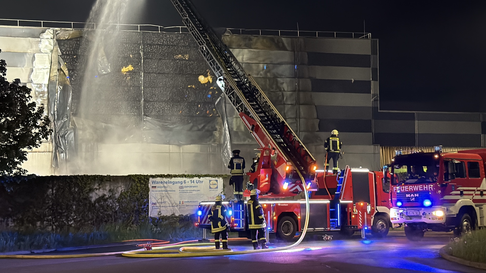 Drehleiter im Löscheinsatz an einer brennenden Lagerhalle bei Nacht